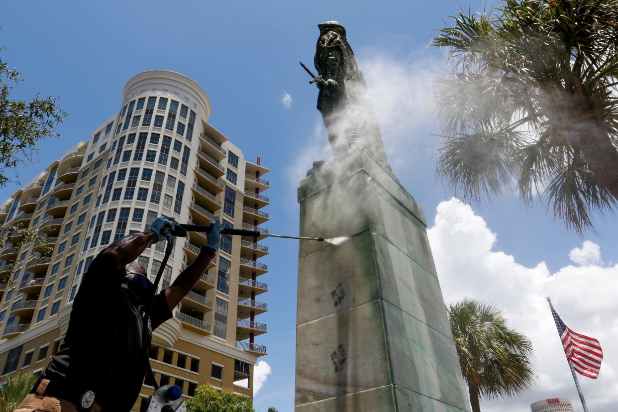 A Hillsborough County employee with the Rapid Response Team removes remaining graffiti on the pedestal of the statue at Columbus Statue Park in Tampa, Fla. on Tuesday, June 30, 2020. A column of black fists lined the sides of pedestal.