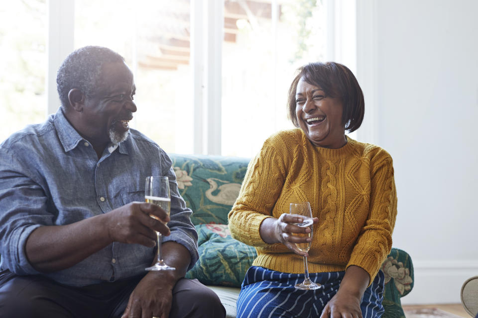 Cheerful male and female friends enjoying champagne while talking at home during Christmas celebration