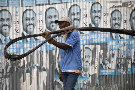 A man carrying metal bars walks past discoloured electoral posters of presidential candidate Jude Celestin in Port-au-Prince, Haiti, January 15, 2016. REUTERS/Andres Martinez Casares