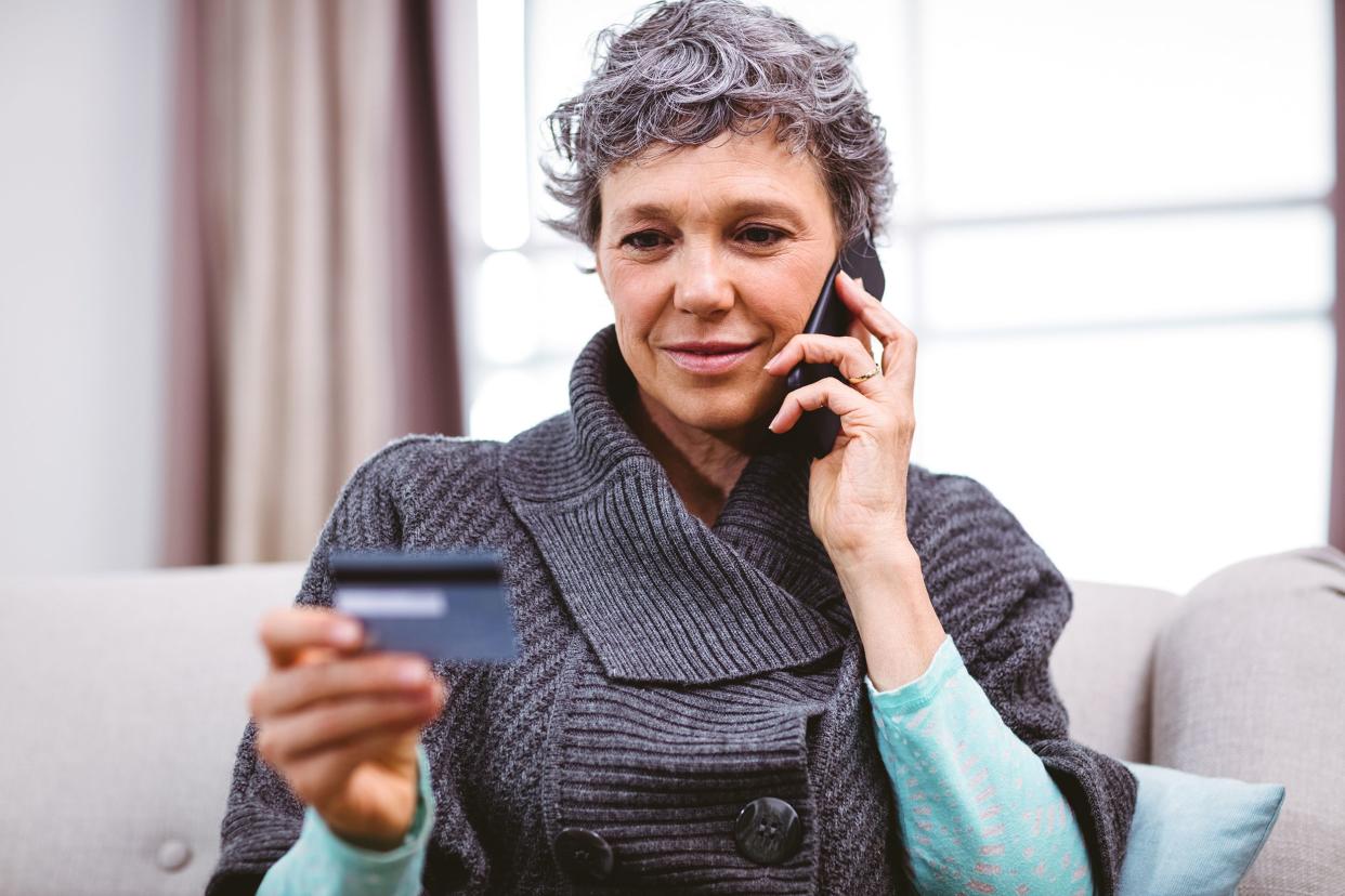 mature woman holding credit card while talking on mobile phone at home