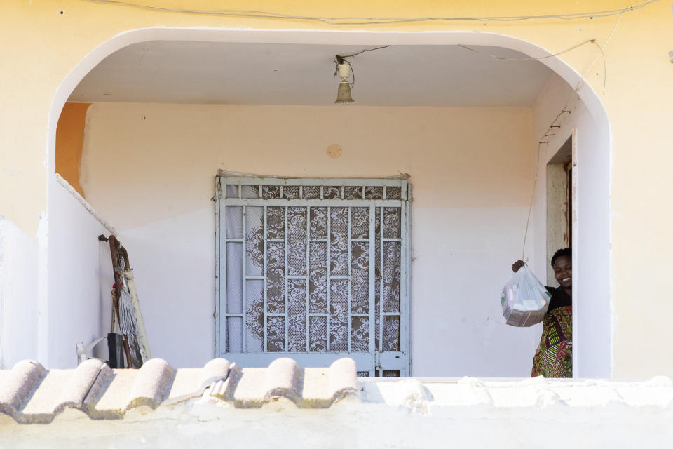 In this photo taken on Monday, April 27, 2020, Mercy Fred, a woman from Nigeria, shows her shopping bags with food while thanking Father Daniele Moschetti for donating them, in Castel Volturno, near Naples, Southern Italy. They are known as “the invisibles,” the undocumented African migrants who, even before the coronavirus outbreak plunged Italy into crisis, barely scraped by as day laborers, prostitutes and seasonal farm hands. Locked down for two months in their overcrowded apartments, their hand-to-mouth existence has grown even more precarious with no work, no food and no hope. (AP Photo/Alessandra Tarantino)