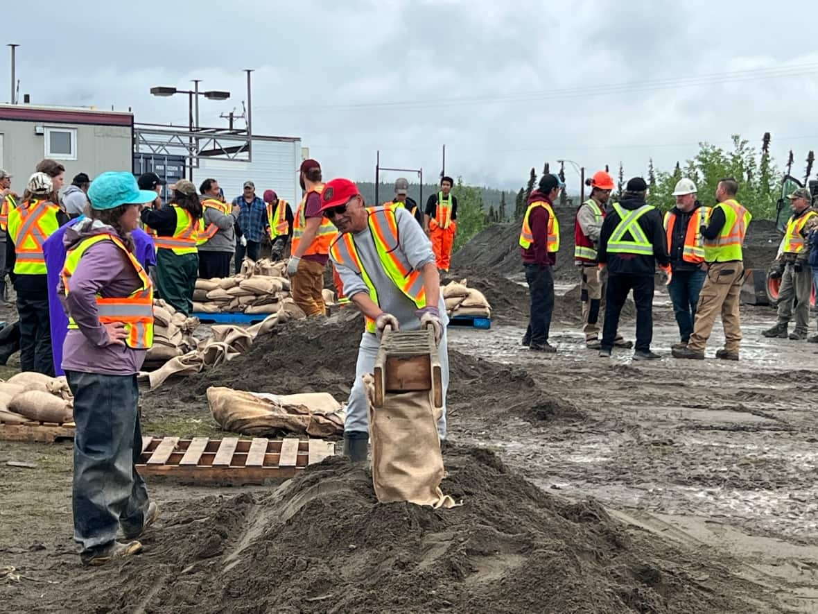 Teslin residents fill sandbags on Tuesday. The deputy chief of the Teslin Tlingit Council said about 65 to 70 people volunteered to help fill and distribute more about 18,000 sandbags on Monday and Tuesday in areas at risk of being flooded in the community. (Mike Rudyk/CBC - image credit)