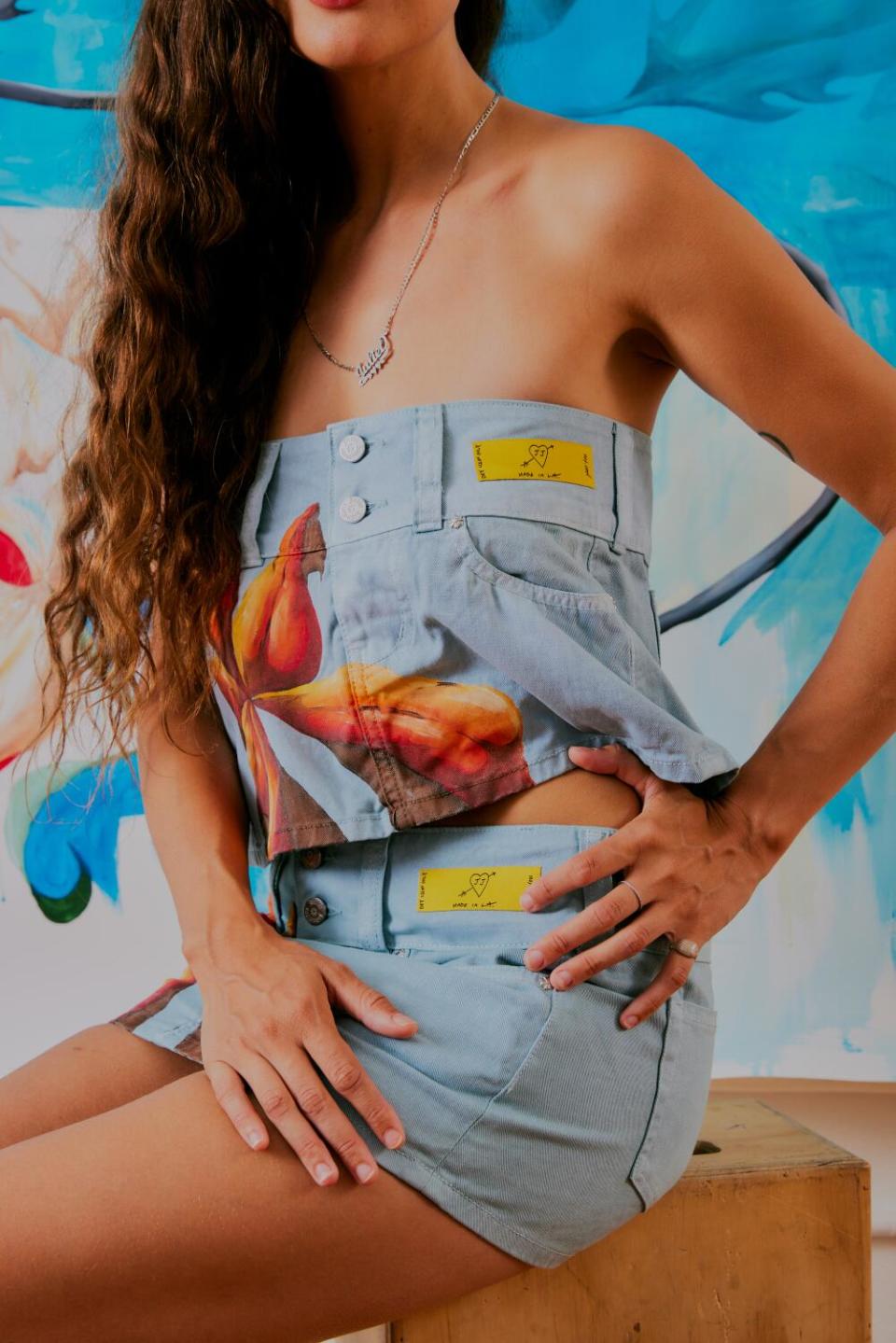 A close-up image of a woman wearing jean shorts as a top and bottom, both painted with orange flowers.