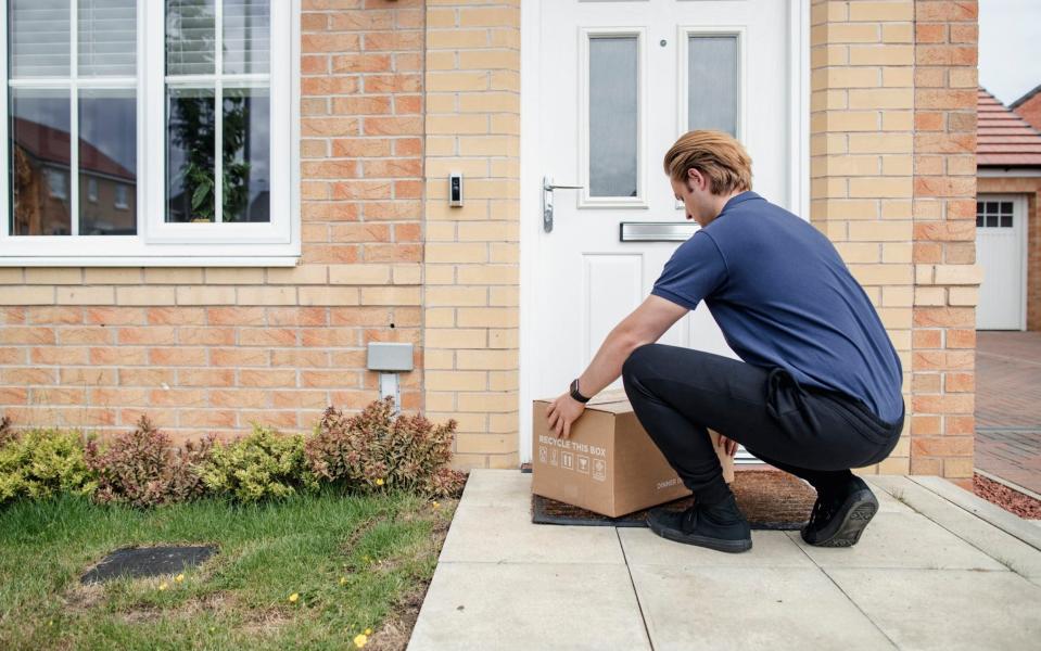 A rear-view shot of a delivery man placing down a package at the front doorstep of a residential house