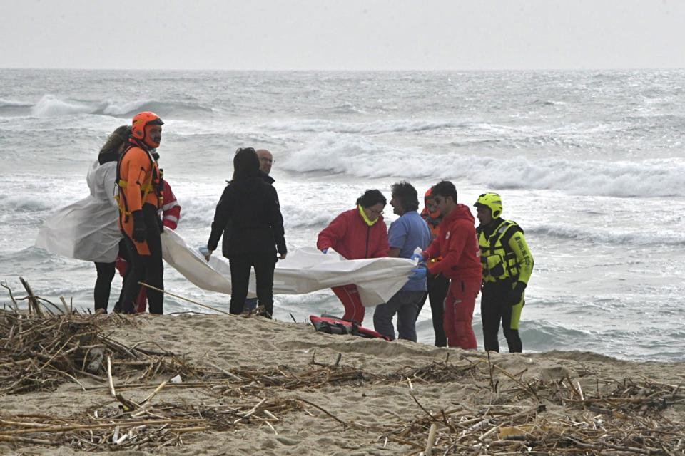 Italian firefighters and Red Cross personnel gather on the beach, surrounded by debris (EPA)