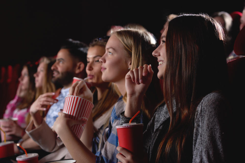 Group of friends smiling and eating popcorn in a movie theater