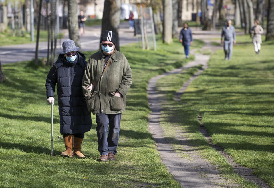 A couple wearing protective face masks walk through The Meadows, Edinburgh, during the sunny Easter bank holiday weekend, as the UK continues in lockdown to help curb the spread of the coronavirus.
