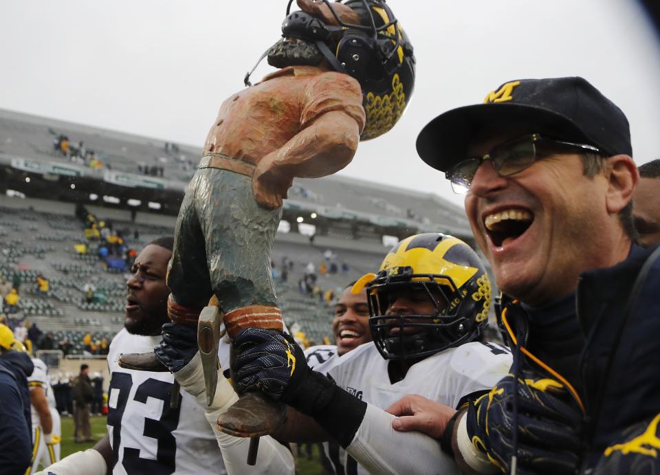 Michigan defensive lineman Lawrence Marshall (93), linebacker Devin Bush, and head coach Jim Harbaugh walk off the field with the Paul Bunyan trophy after an NCAA college football game against Michigan State, Saturday, Oct. 20, 2018, in East Lansing, Mich. Michigan won 21-7. (AP Photo/Carlos Osorio)