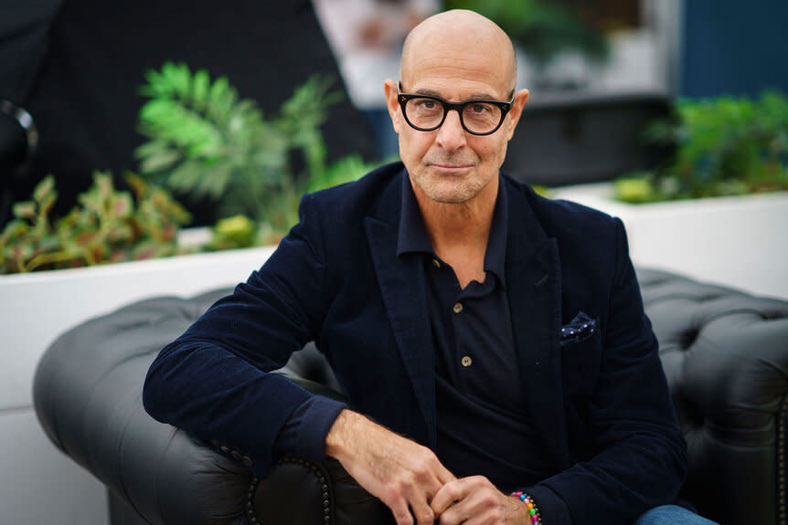 Stanley Tucci sits in a pose while looking at the camera