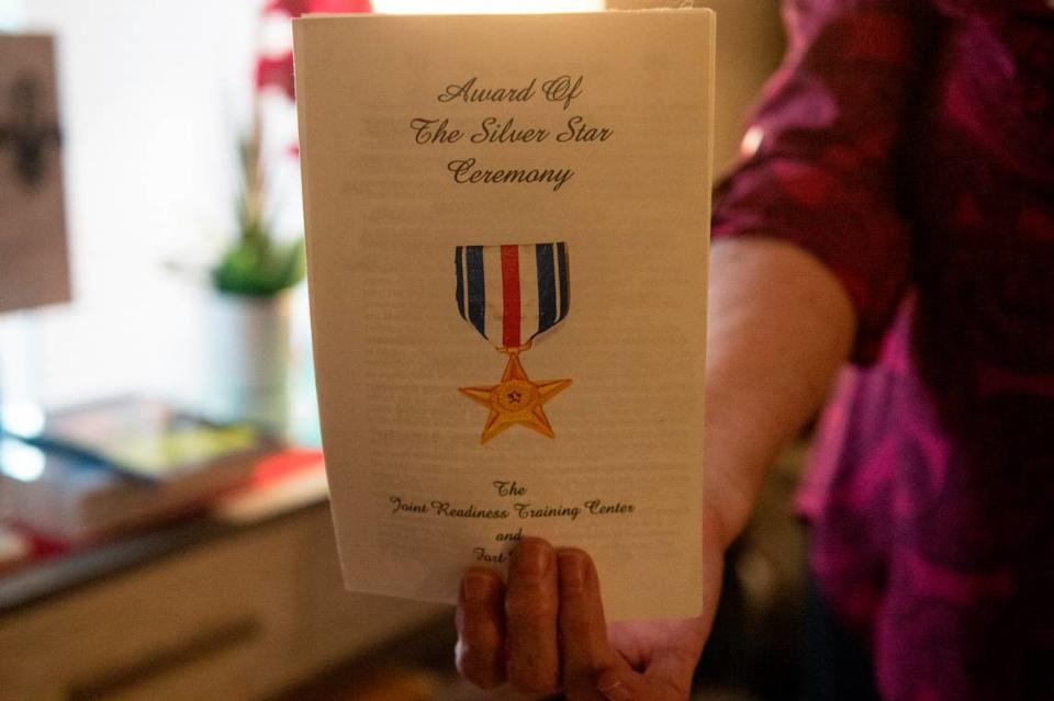 Deborah Tainsh, an author and gold star mother, holds up the program from the Silver Star ceremony for her son, Patrick, at her home in Biloxi on Wednesday, Nov. 8, 2023. Patrick, who died fighting in Iraq, inspired her to write.