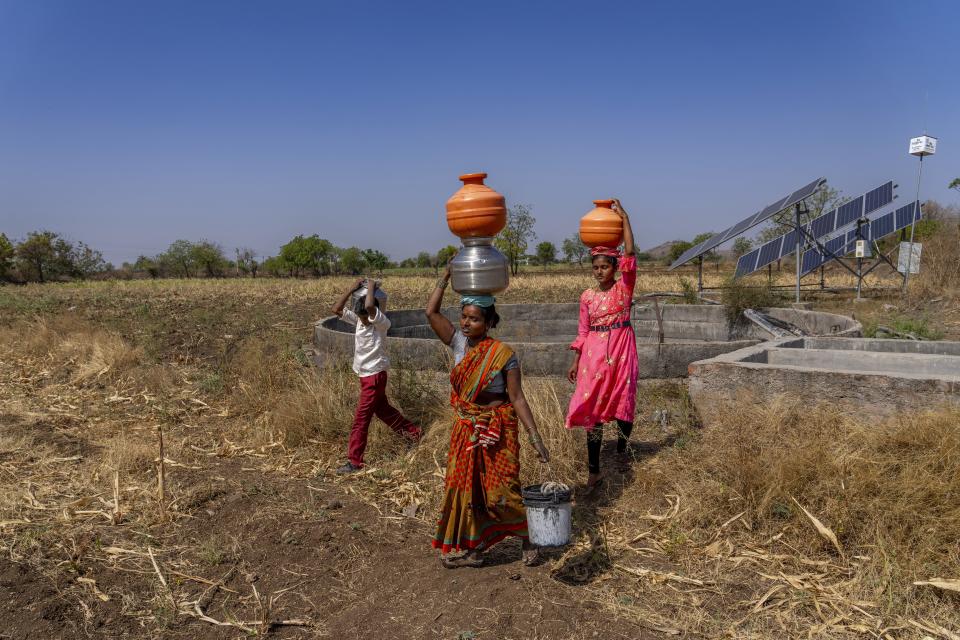A woman along with her kids carry their vessels filled with water that they collected from a well in Shirur Kasar village, Beed district, India, Sunday, May 5, 2024. (AP Photo/Rafiq Maqbool)