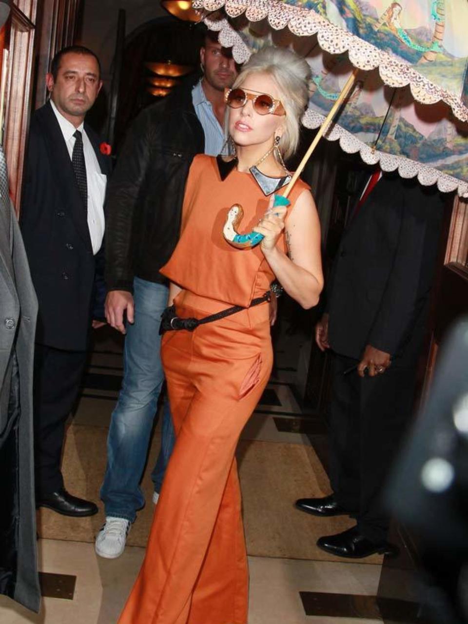 <p>Lady Gaga goes for bold in this tangerine top with wide leg trousers complete with round sunglasses and printed umbrella in London, November 2012.</p>