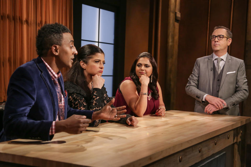 Four people having a discussion around a wooden counter, likely on a talk show or panel