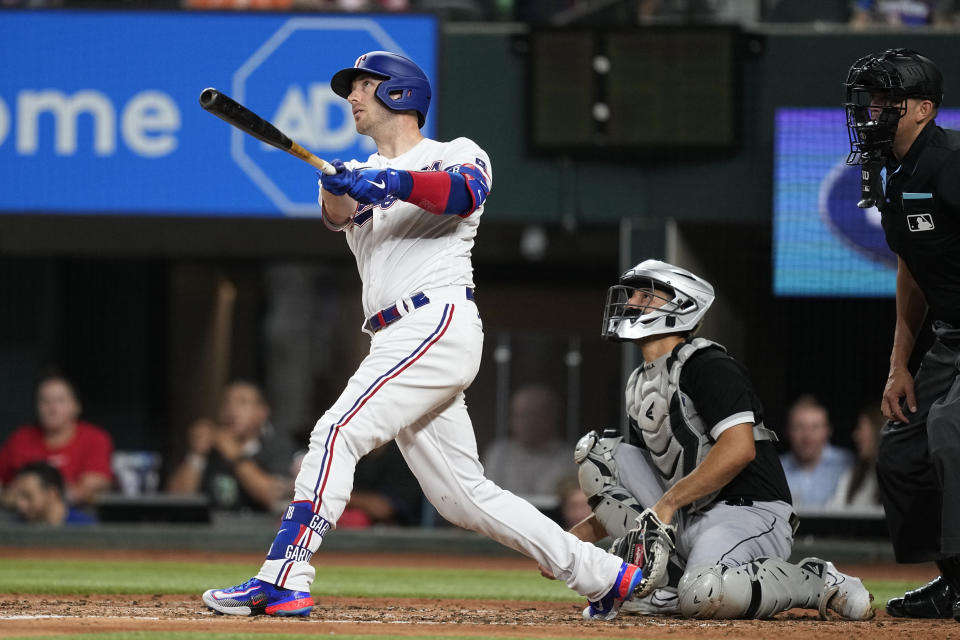 Texas Rangers' Mitch Garver follows through on a solo home run swing as Chicago White Sox catcher Seby Zavala and umpire Emil Jimenez, right, look on in the fifth inning of a baseball game, Tuesday, Aug. 1, 2023, in Arlington, Texas. (AP Photo/Tony Gutierrez)
