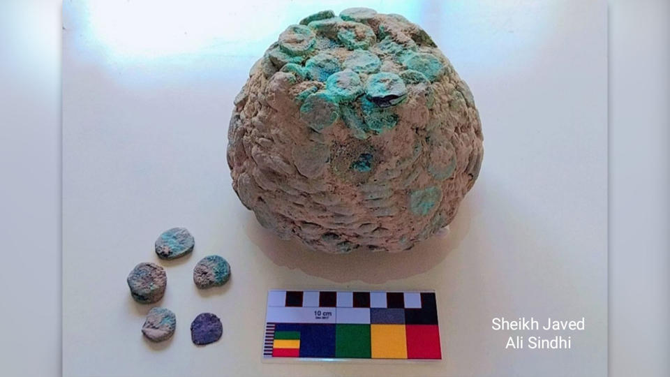 Hoard of copper coins tarnished green and fused together into a single lump with five additional coins on a white display.