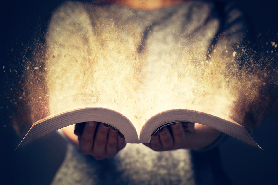 Woman holding an open book bursting with light.