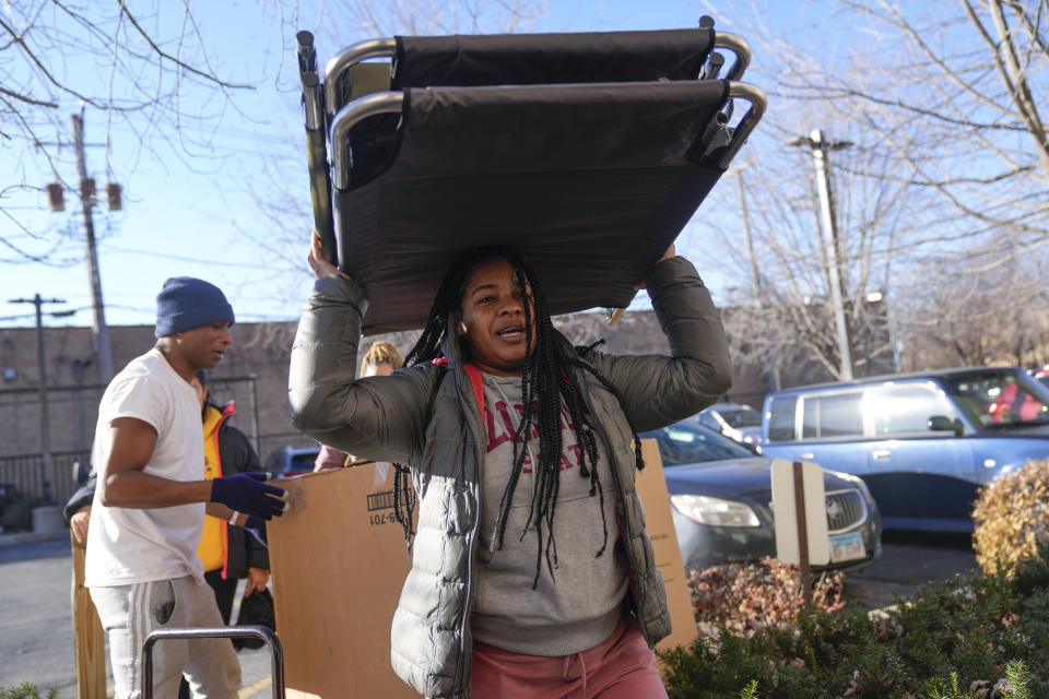 Yimara Pajaro of Venezuela carries cots into the Chicago City Life Center, Nov. 29, 2023, in Chicago. Gov. J.B. Pritzker’s administration on Tuesday, Dec. 5 announced it is scrapping construction of the temporary winter camp for migrants, citing the risk of contaminants at the former industrial site. (AP Photo/Erin Hooley)