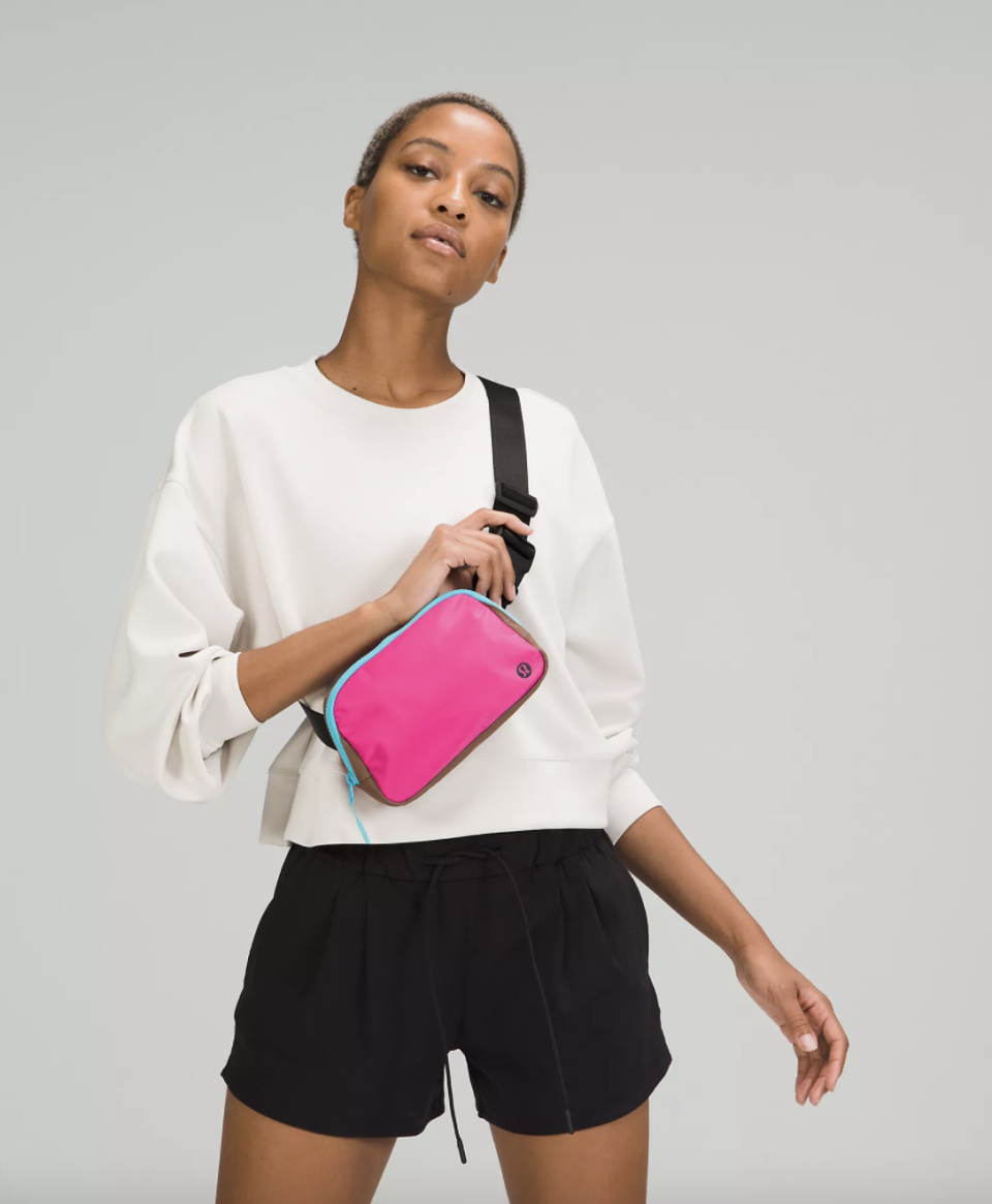 model wearing white shirt and black shorts wearing lululemon Everywhere Belt Bag in bright pink