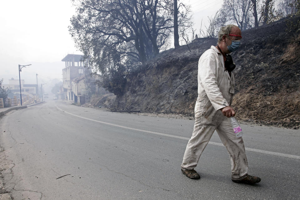 A man leaves a village near Tizi Ouzou some 100 km (62 miles) east of Algiers following wildfires in this mountainous region, Tuesday, Aug.10, 2021. Firefighters were battling a rash of fires in northern Algeria that have killed at least six people in the mountainous Kabyle region, the interior minister said Tuesday, accusing "criminal hands" for some of the blazes. (AP Photo/Fateh Guidoum)