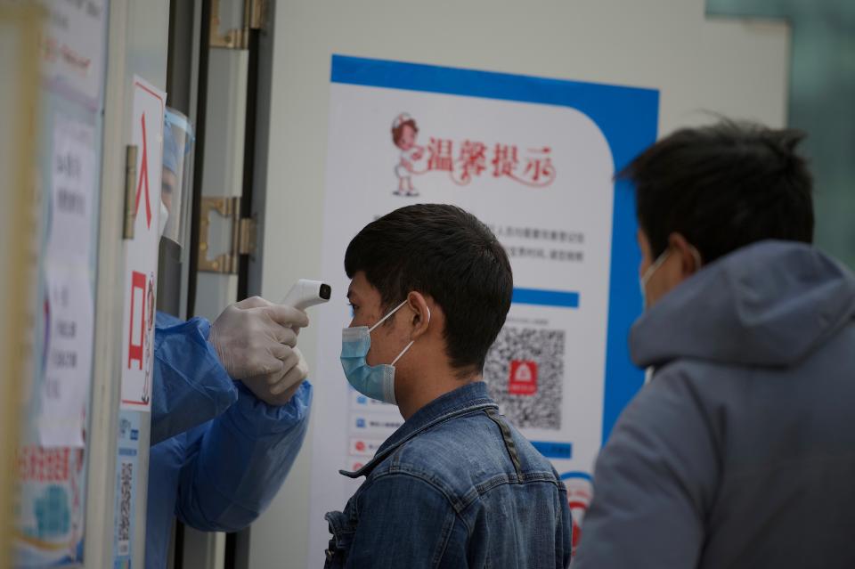 A medical worker checks the temperature of people getting nucleic acid tests at a hospital in the Daxing district of Beijing on January 22, 2021, after a partial lockdown was imposed on the Chinese capital 