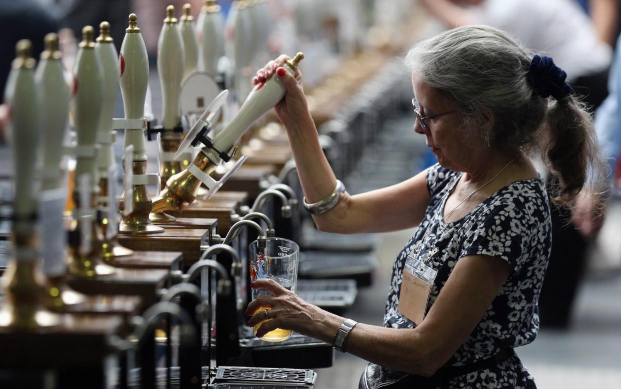 A woman pulls a pint of beer behind a bar in the Great British Beer Festival in the Olympia exhibition centre