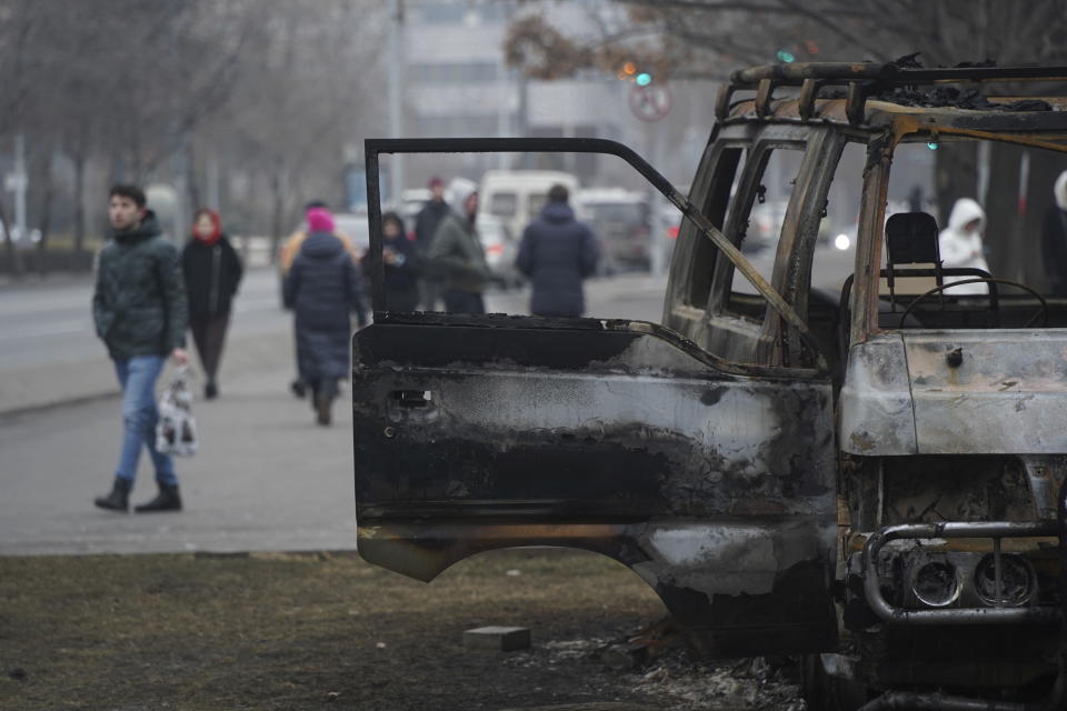 People walk past a bus, which was burned during clashes in Almaty, Kazakhstan, Tuesday, Jan. 11, 2022. Life in Almaty, which was affected with the violence the most during protests, started returning to normal this week, with public transport resuming operation and malls reopening. (Vladimir Tretyakov/NUR.KZ via AP)