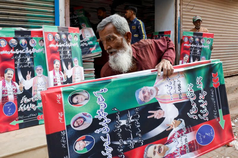 A worker carries campaign posters of a political party to decorate the area, ahead of general elections, in Karachi