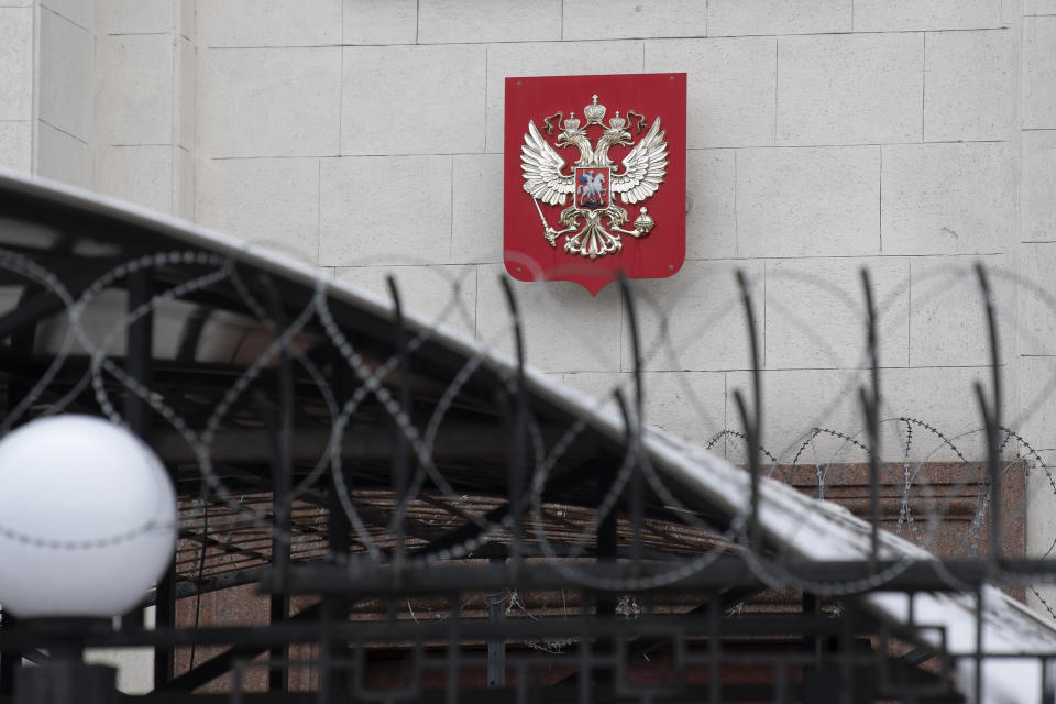 The emblem of Russia is seen through the barbed wire on the building of the Russian Embassy in Kyiv, Ukraine, Saturday, Feb. 12, 2022. Maria Zakharova, a Russian Foreign Ministry spokeswoman said her country had "optimized" staffing at its own embassy in Kyiv in response to concerns about possible military actions from the Ukrainian side. (AP Photo/Andrew Kravchenko)