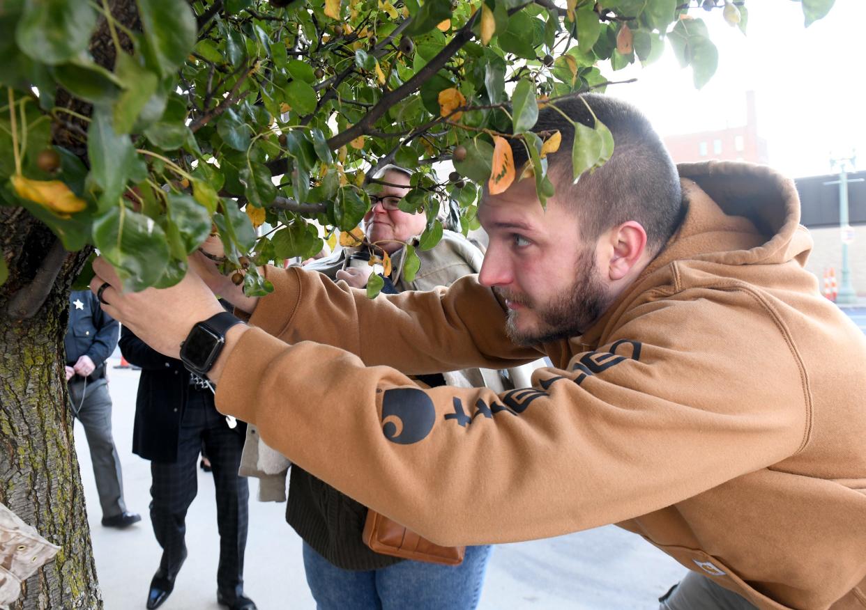 Bryce Husted, a probation officer with Stark County Honor Court, hangs a dog tag on the witness tree outside the Stark County Courthouse on Tuesday to remember a veteran who died by suicide.