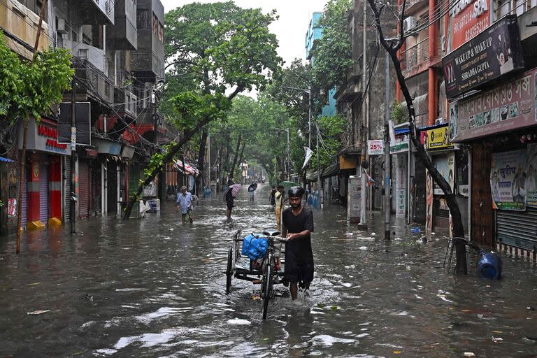 Un hombre empujando un carro de tres ruedas camina por una calle inundada durante la lluvia en Calcuta el 27 de mayo de 2024, tras la llegada del ciclón Remal en el estado de Bengala Occidental en la India.