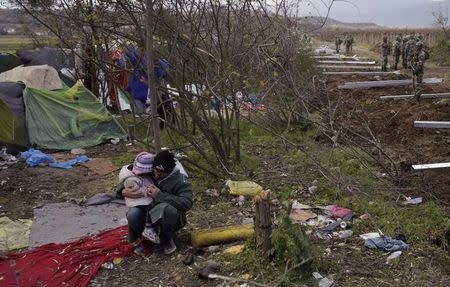 A migrant sits with his child as Macedonian soldiers start to erect a metal fence on the border with Greece, near Gevgelija, Macedonia, November 28, 2015. REUTERS/Stoyan Nenov