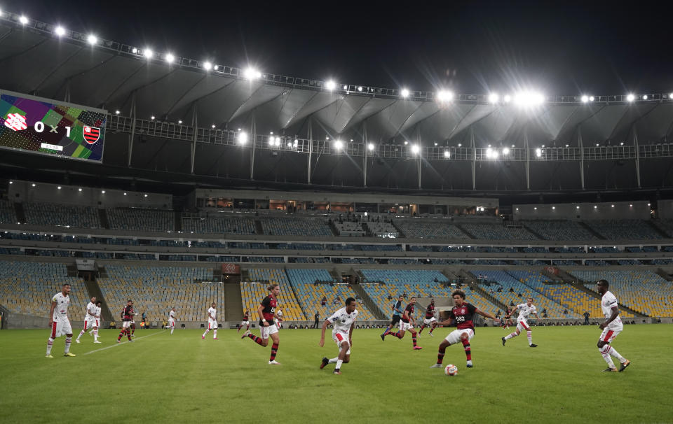 Players of Bangu, wearing white uniforms, and Flamengo play a Rio de Janeiro soccer league match at the Maracana stadium in Rio de Janeiro, Brazi, Thursday, June 18, 2020. Rio de Janeiro's soccer league resumed after a three-month hiatus because of the coronavirus pandemic. The match is being played without spectators to curb the spread of COVID-19. (AP Photo/Leo Correa)