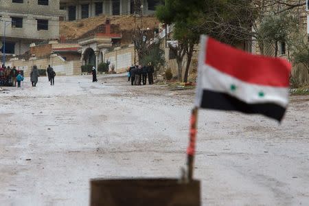 A Syrian national flag flutters near residents who said they have received permission from the Syrian government to leave the besieged town as they wait with their belongings after an aid convoy entered Madaya, Syria, January 14, 2016. REUTERS/Omar Sanadiki