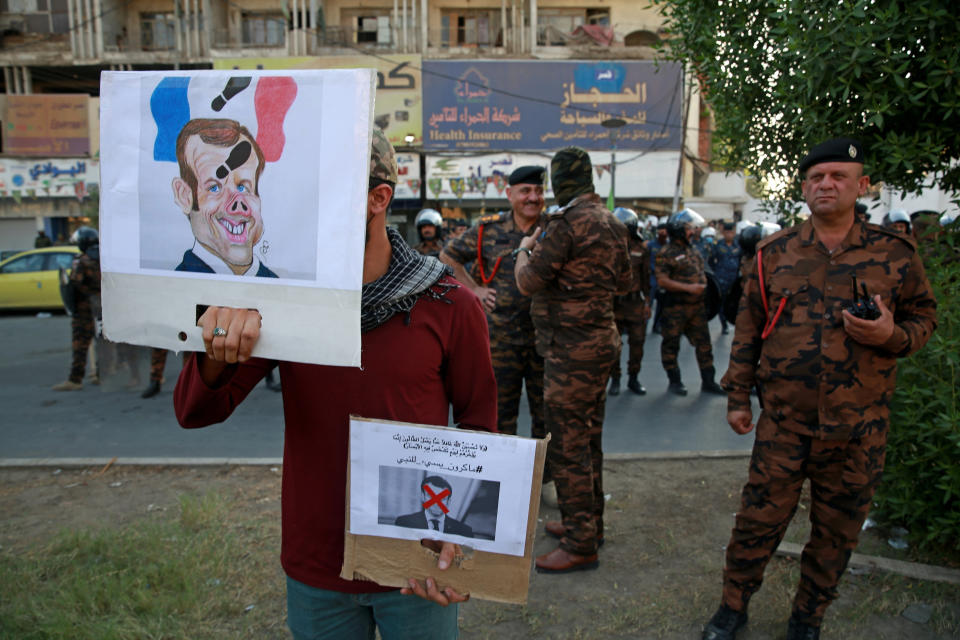 A protester holds defaced pictures of French President Emmanuel Macron during a protest over caricatures of the Prophet Muhammad they deem insulting and blasphemous, outside the French Embassy, in Baghdad, Iraq, Monday, Oct. 26, 2020. Muslims in the Middle East and beyond on Monday called for boycotts of French products and for protests over the caricatures, but France's president has vowed his country will not back down from its secular ideals and defense of free speech. (AP Photo/Khalid Mohammed)