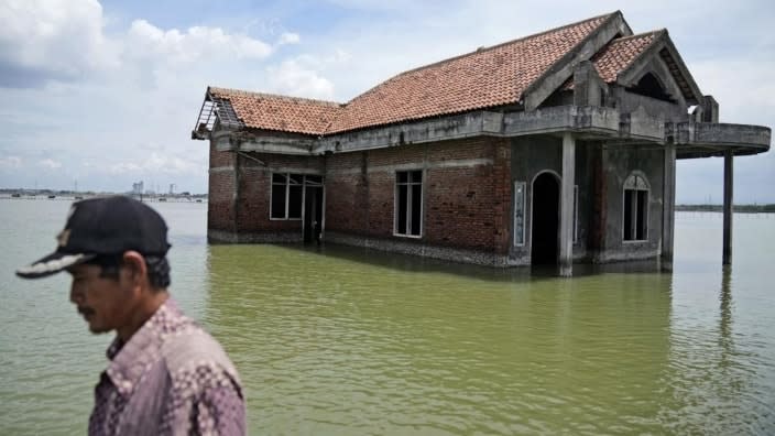 A man walks past a house abandoned after it was inundated by water due to the rising sea level in Sidogemah, Central Java, Indonesia. (Photo: Dita Alangkara/AP, File)