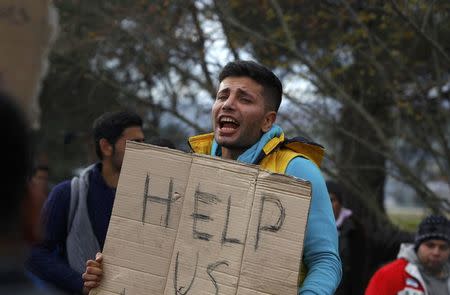 A migrant holds a poster, as he waits to cross the border from Greece to Gevgelija, Macedonia November 22, 2015. REUTERS/Ognen Teofilovski