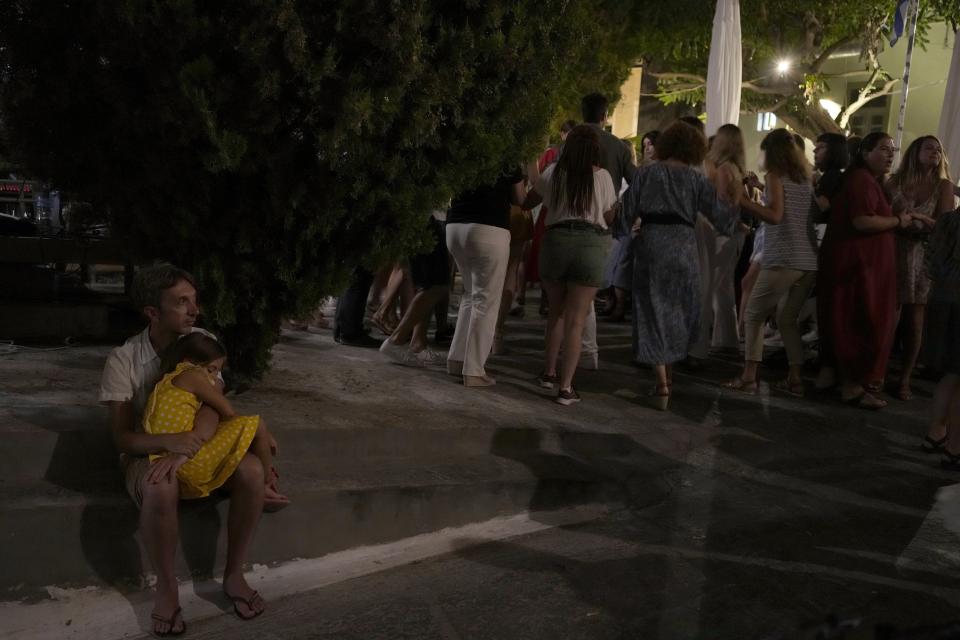 A man holds a girl as she sleeps during a festivity, known as Panigiri, on the Aegean Sea island of Tzia or Kea, Greece, early Tuesday, Aug. 16, 2022. The Dormition of the Virgin Mary (or Mother of God as the Greeks usually refer to her) is celebrated on Aug. 15. The religious event is coupled with midsummer festivities, known as Panigiria, that often last more than a day with music, culinary feasts and, in many cases, flea markets. (AP Photo/Thanassis Stavrakis)