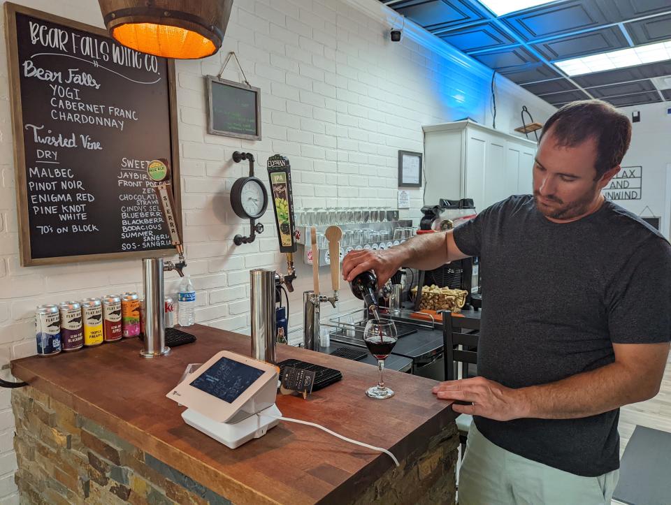 Alan Jones, the new owner of Bear Falls Wine Company on Hendersonville's Main Street, pours a glass of red wine at the shop's counter.