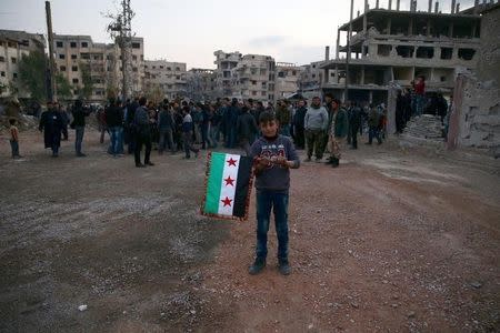 A boy carries an opposition flag as rebel fighters and civilians gather during the arrival of an aid convoy of Syrian Arab Red Crescent and United Nation (UN) to the rebel held besieged town of Kafr Batna, on the outskirts of Damascus, Syria February 23, 2016. REUTERS/Bassam Khabieh