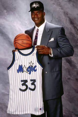 <p>Brian Drake/NBAE via Getty</p> Shaquille O'Neal poses for a portrait with his #33 Orlando Magic jersey after being drafted in 1992.