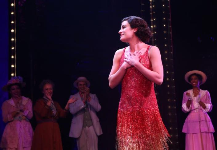 A woman in a sparkly red dress with fringe pressing her hands to her chest on a stage
