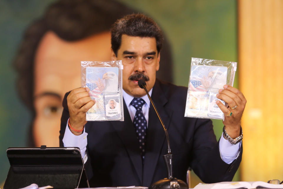 In this photo released by Venezuela's Miraflores presidential press office, President Nicolas Maduro shows what Venezuelan authorities claim are identification documents of former U.S. special forces and U.S. citizens Airan Berry, right, and Luke Denman, left, during a online press conference in Caracas, Venezuela, Wednesday, May 6, 2020. Maduro also touted a video showing a scruffy-looking Texas native Luke Denman, divulging details about a failed invasion as proof that U.S. authorities backed an attempt to forcibly remove him from power. (Miraflores Palace presidential press office via AP)