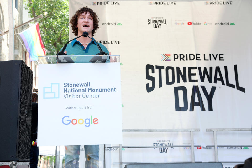 Zander Moricz, a young man with curly brown hair that is speaking at a podium on a stage. The podium says "Stonewall National Monument" and "Google." the stage says "Stonewall Day"