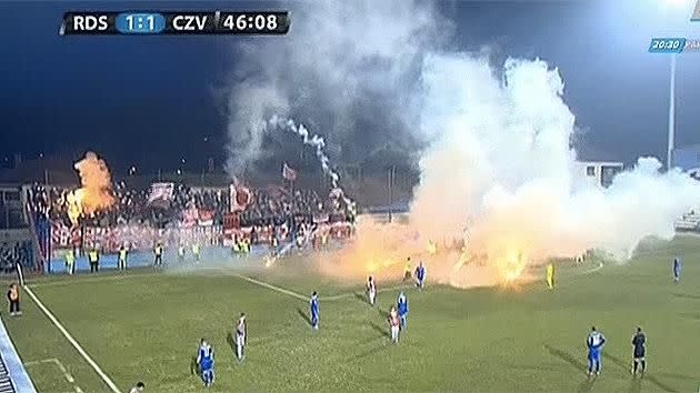 Players were forced to stand around as flares continued to hit the pitch. Pic: YouTube