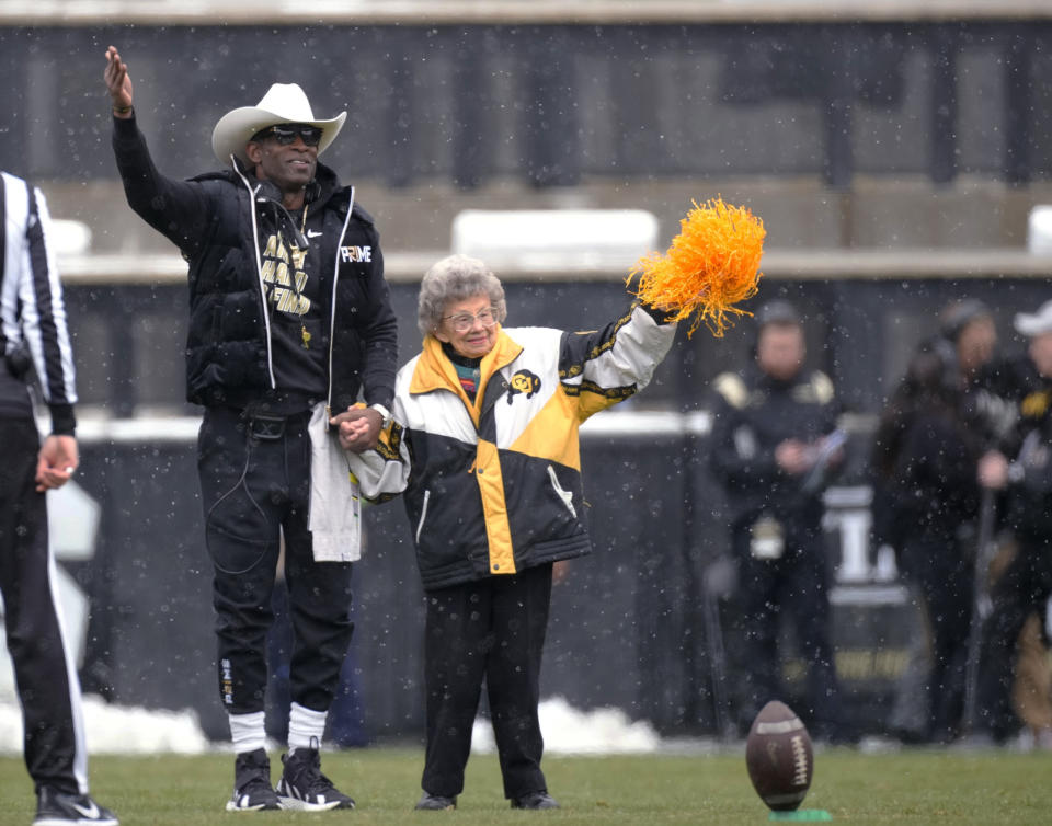 FILE - Colorado coach Deion Sanders, left, leads longtime supporter Peggy Coppom to kick the football before the team's spring practice NCAA college football game April 22, 2023, in Boulder, Colo. Coppom, who turns 99 on Sunday, is royalty. She’s a fixture at Buffaloes football and basketball games and couldn’t be more elated that after a 13-season move to the Pac-12, the school is making the switch back to the Big 12 next year. She does lament, though, that traditional conference rival Nebraska has moved on the Big Ten. (AP Photo/David Zalubowski, File)