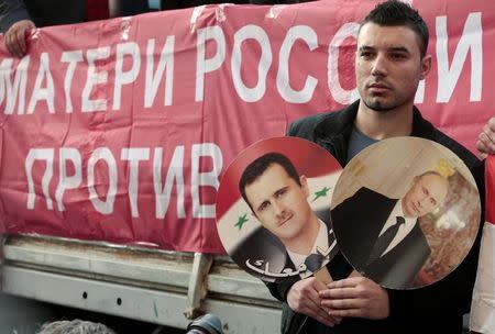 A participant hold images of Russian President Vladimir Putin and Syrian President Bashar al-Assad during an anti-war protest organised by the Communist party near the U.S. embassy in Moscow in this September 12, 2013 file photo. REUTERS/Tatyana Makeyeva