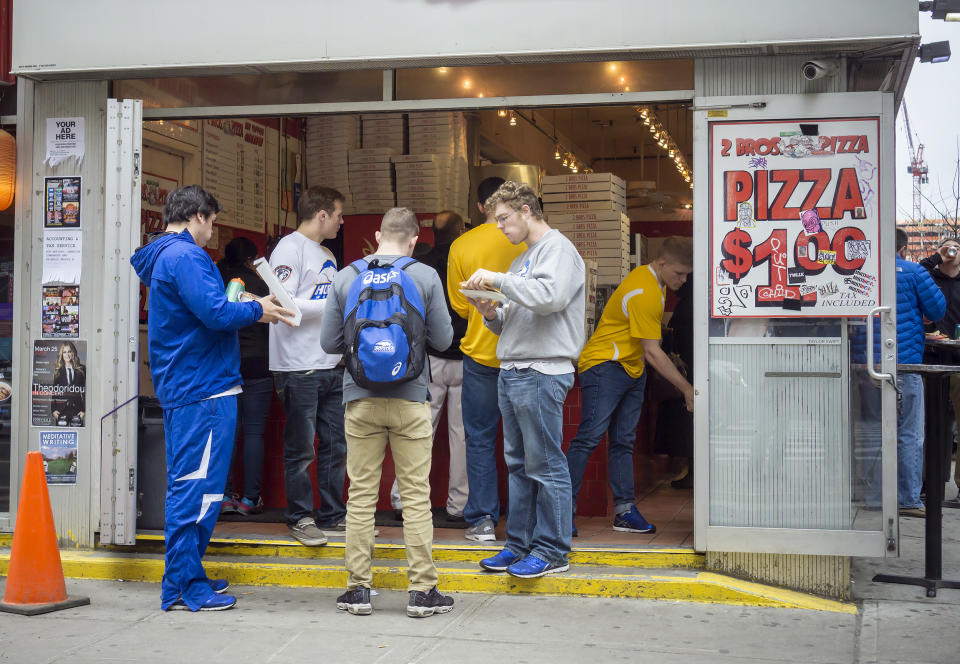 A group of guys eat dollar pizza at 2 Bros Pizza in NYC. (Richard Levine / Getty Images)