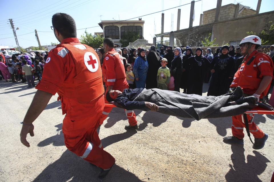 Lebanese Red Cross workers carry an injured man who was wounded by the Syrian government forces, as they pass in front of Lebanese and Syrian women in the main square of Tfail village, at the Lebanese-Syrian border, eastern Lebanon, Tuesday April 22, 2014. A Lebanese convoy of soldiers, clerics and Red Cross officials delivered aid Tuesday to a remote village near the Syrian border that was bombed by Syrian government aircraft and blocked by Lebanese militants fighting alongside President Bashar Assad’s forces in the civil war next door. Hezbollah fighters have been patrolling the area on the Lebanese side and fighting has flared up inside Syria, cutting Tfail’s residents off from all sides for months. (AP Photo/Hussein Malla)