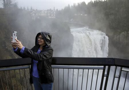 A woman poses for a photo in front of Snoqualmie Falls after recent storms increased water flow in Snoqualmie, Washington, December 10, 2015. REUTERS/Jason Redmond