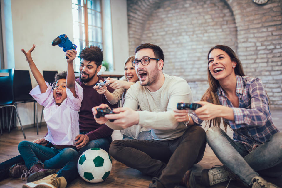 A family plays video games together sitting on the floor.